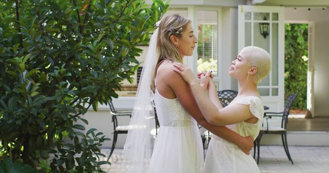 Lesbian couple sharing a moment dancing at their beautiful intimate backyard wedding. Brides wearing elegant white dresses, surrounded by garden greenery and serene atmosphere. Perfect for illustrating love, diversity, and inclusive celebrations in advertisements, wedding planning websites, and LGBTQ rights campaigns.