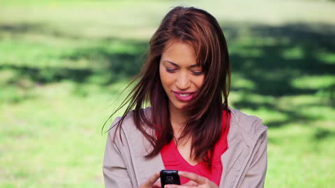 Smiling Woman Texting on Smartphone in Sunny Park