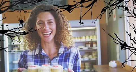 Cheerful Woman Displaying Cupcakes in a Halloween-Themed Bakery