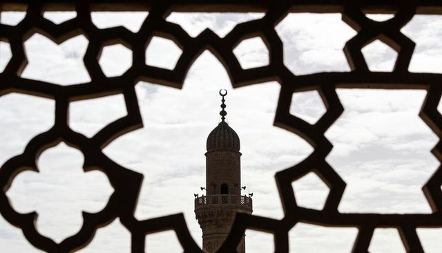 Framing minaret through ornate geometric lattice, crescent finial silhouette against sky