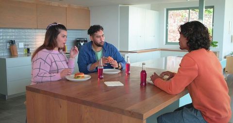 Multicultural friends chatting and eating burgers at bright modern kitchen island