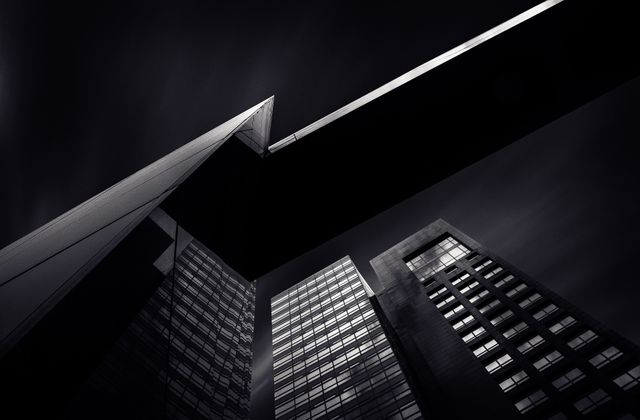 This image features modern architectural structures with dramatic lighting against a dark sky. The perspective emphasizes the height and sleek design of the glass facade skyscrapers, ideal for use in projects related to urban living, corporate themes, modern design, architectural presentations, and city mood backgrounds.