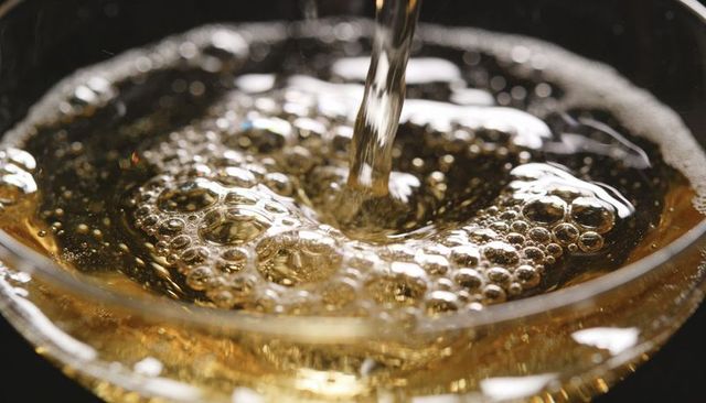 Pouring amber sparkling drink into stemmed glass forming whirlpool and bubbles