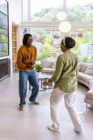 African american couple dancing and laughing in bright modern living room with garden view