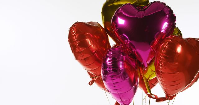 A cluster of shiny red and gold heart-shaped balloons floats against a bright background, with copy space. These balloons are often used to symbolize love and celebration during special occasions like Valentine's Day or anniversaries.