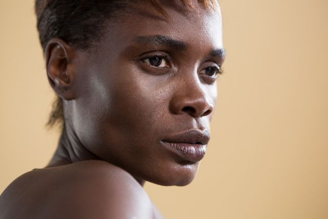 Close-up of an androgynous person with a thoughtful expression against a beige background. Ideal for use in articles or campaigns focusing on gender identity, emotions, human expressions, and diversity. Can be used in blogs, magazines, or social media posts discussing introspection, neutrality, and personal reflection.