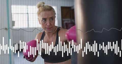 Woman punching heavy bag wearing pink gloves during intense boxing workout session