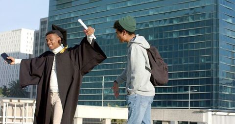 Young african american graduate celebrating on urban rooftop with friend holding diploma