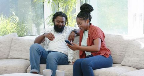 African American Couple Relaxing on Sofa Sharing Smartphone in Bright Living Room