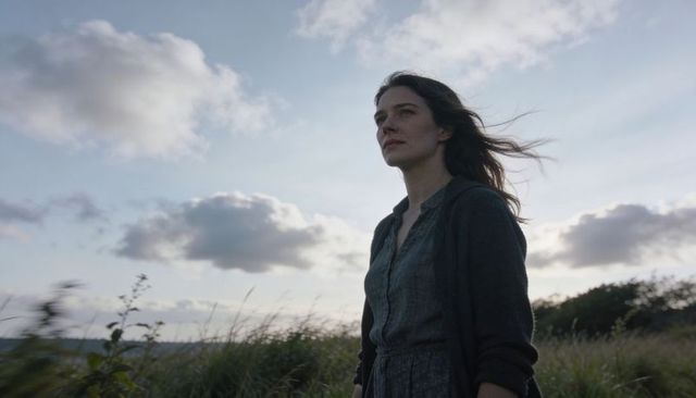 Gazing woman standing in windy meadow at dusk, contemplative portrait for wellness travel