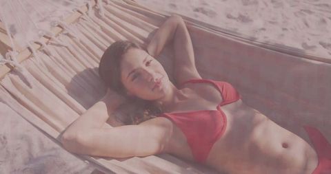 Woman relaxing in red bikini on hammock in sunny beach setting