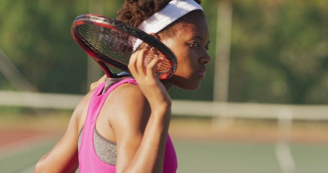 The photo features an African-American female tennis player holding a racket over her shoulder during a pause in an outdoor match. The image captures her focus and determination. Perfect for promoting sports events, athletic gear, women's empowerment, or active lifestyle campaigns.