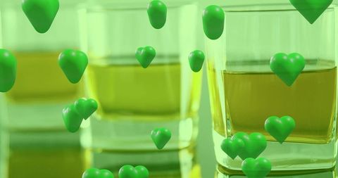 Floating green heart bubbles surrounding amber drink in square glass on reflective surface