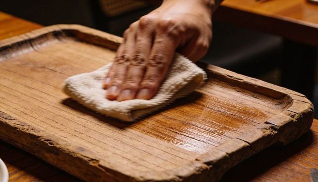 Hand wiping worn wooden tray with terry cloth leaving oil sheen on rustic woodgrain