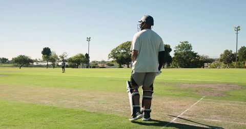 Cricketer walking to crease wearing helmet and pads on suburban cricket ground
