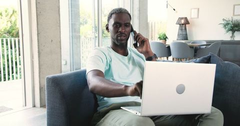 Professional man balancing smartphone and laptop in modern living room