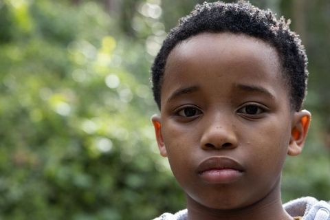 Close-up african american preteen boy looking serious outdoors with bokeh green background