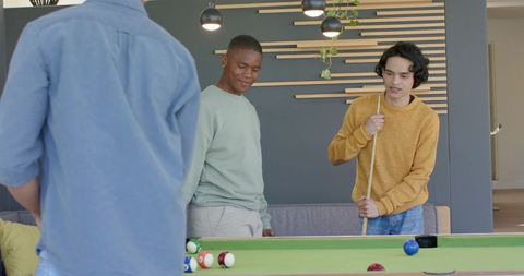 Diverse friends playing pool in modern lounge with green-felt table and warm lighting