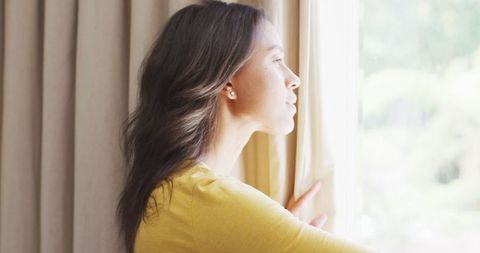 Thoughtful Young Woman Looking Out of Window in Sunny Room