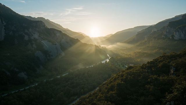 Sunrise rays flooding misty alpine valley with winding river and forest ridges at dawn
