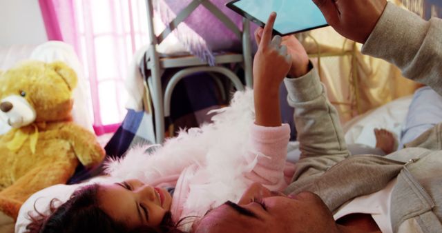 Father and daughter enjoying quality time indoors, playing with a tablet. Perfect for use in articles or promotions about family bonding, parenting, or technology in family life.