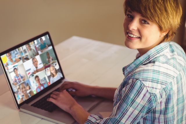 Young person smiling while participating in a virtual meeting on a laptop. Suitable for illustrating concepts of online communication, remote working, digital learning, virtual events, and social networking.