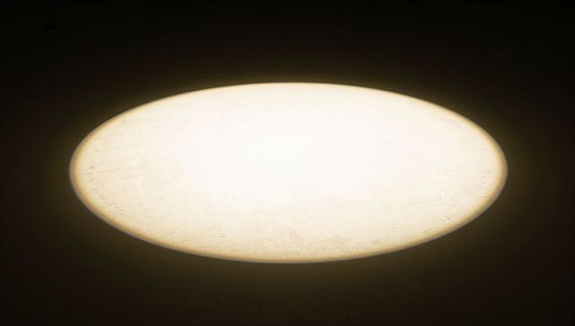 Oval warm spotlight casting on dark floor with textured concrete and minimalist contrast