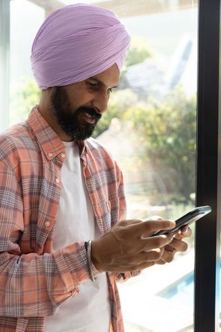 Man in Turban Using Smartphone by Glass Door at Home