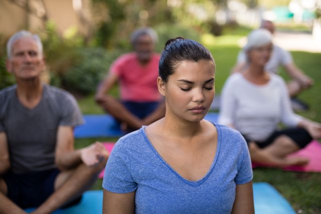 Group of seniors and a trainer meditating outdoors in a park. Ideal for use in wellness, fitness, and health-related content, promoting outdoor activities, mindfulness, and senior fitness programs.