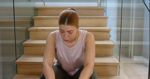 Young woman sitting on wooden stairs catching breath with heart monitor overlay on glass