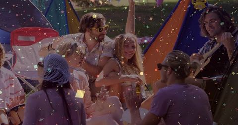 Laughing friends enjoying outdoor music festival picnic with tents, guitar and sunshine