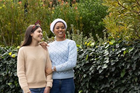Multicultural friends smiling in garden wearing sweaters, santa hat and festive headband sharing hap