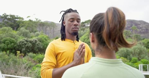 Diverse couple meditating on balcony overlooking green hillside for mindfulness