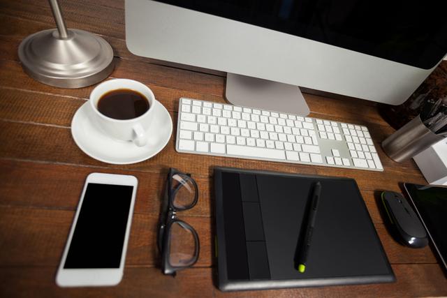 Organized office desk with computer, mobile phone, coffee cup, glasses, digital tablet, and keyboard on a wooden surface. Ideal for business, productivity, workspace, office lifestyle, remote work, or workplace organization themes.