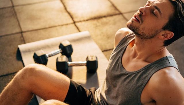 Post-workout man resting on exercise mat with hex dumbbells in warm golden light