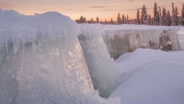 Glowing frozen waterfall and clear ice sheets catching pastel sunrise over snowy gorge