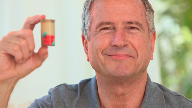 Senior man holding pill container and smiling, symbolizing good health and wellness. Useful for healthcare and pharmaceutical advertisements, senior healthcare services promotion, articles on elderly health and wellness, or retirement community promotional materials.