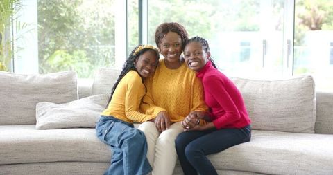 African American Mother and Daughters Smiling and Embracing on Bright Living Room Sofa