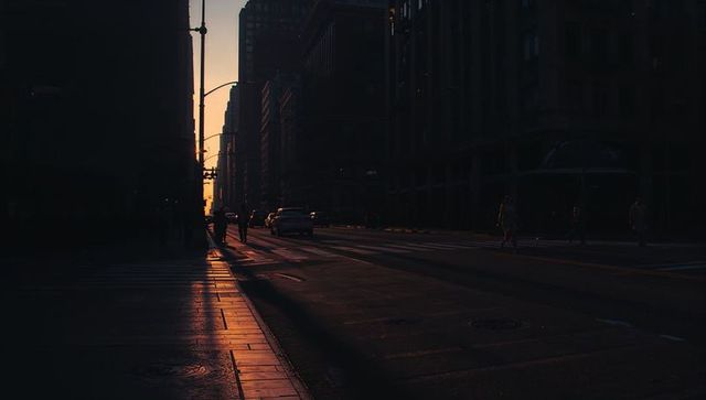Sunset silhouette on urban street with warm sidewalk reflection and moody city canyon