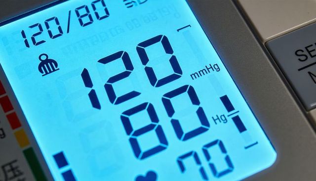 Backlit digital blood pressure monitor displaying 120/80 mmhg on blue lcd closeup