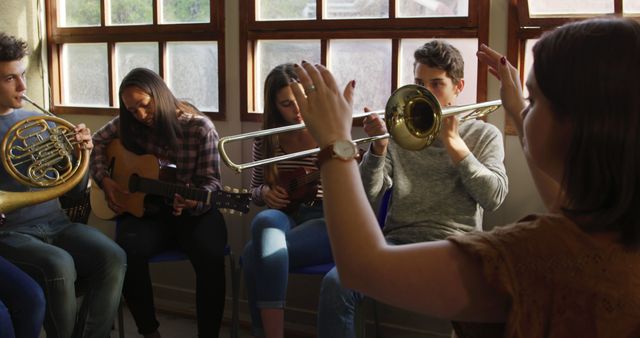 Group of teenagers playing various musical instruments, including guitar, trombone, and French horn, in a classroom. This showcases a creative and educational setting, ideal for promoting music education, teamwork, and youth programs.