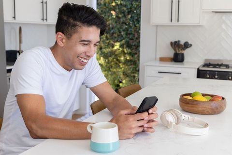 African american man smiling, texting on smartphone at bright minimalist kitchen island