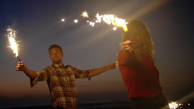 Couple enjoying a playful moment with sparklers at the beach during sunset, creating a romantic and joyful atmosphere. Perfect for depicting lively celebrations, romantic getaways, or carefree moments during vacations. Great for use in travel brochures, lifestyle blogs, or festive advertisements highlighting happiness and togetherness.