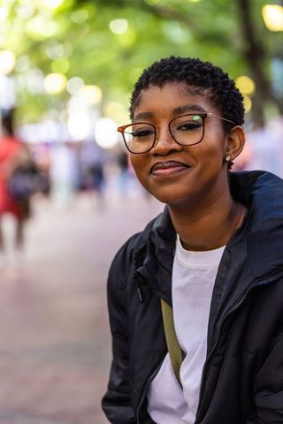 Smiling african american woman wearing glasses on tree-lined urban promenade with bokeh