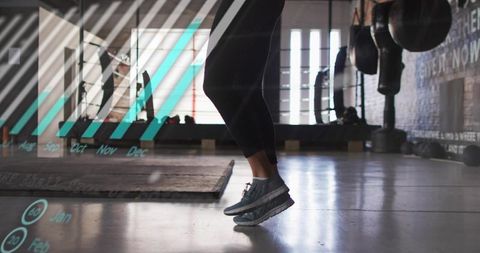 Woman jumping in gym wearing gray sneakers and black leggings with teal data overlay