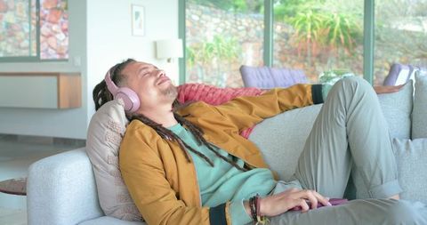 Young man relaxing on sofa with pink headphones and smartphone in sunlit cozy living room