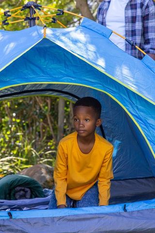 African american child camping in blue pop-up tent with guardian at sunny forest campsite