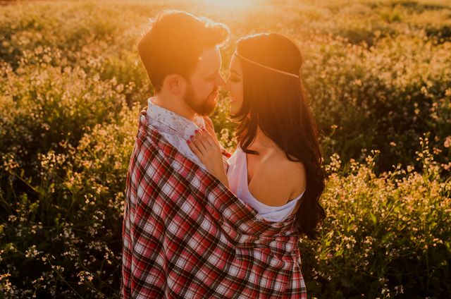 Young couple embracing amid sunlit meadow, wrapped in plaid blanket. The moment showcases love, intimacy, and happiness in a natural, outdoor setting. Perfect for use in relationship-themed advertisements, romance book covers, or lifestyle blogs, emphasizing connection and natural beauty.