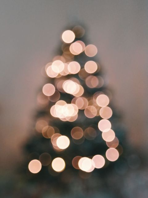 This image features a blurred Christmas tree with warm glowing lights, creating a beautiful bokeh effect. The soft focus makes it suitable for use as a festive background or overlay for holiday greetings, advertisements, or decorations. Ideal for web and print designs requiring a warm and celebratory ambiance.