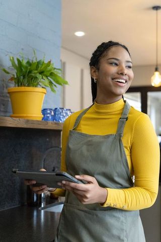 Smiling barista holding tablet in modern cafe wearing mustard turtleneck and apron